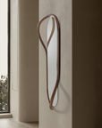 Decorative wall mirror with wooden frame leaning against a wall next to a window.