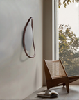Wooden chair with woven backrest in a room with a large window showing greenery outside.