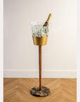 Gold and bronze drink cooler with ice and a bottle on a wooden floor.