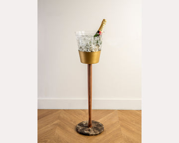 Gold and bronze drink cooler with ice and a bottle on a wooden floor.
