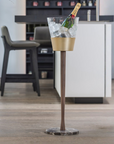 Clear ice bucket with gold base on a stand in a bar setting