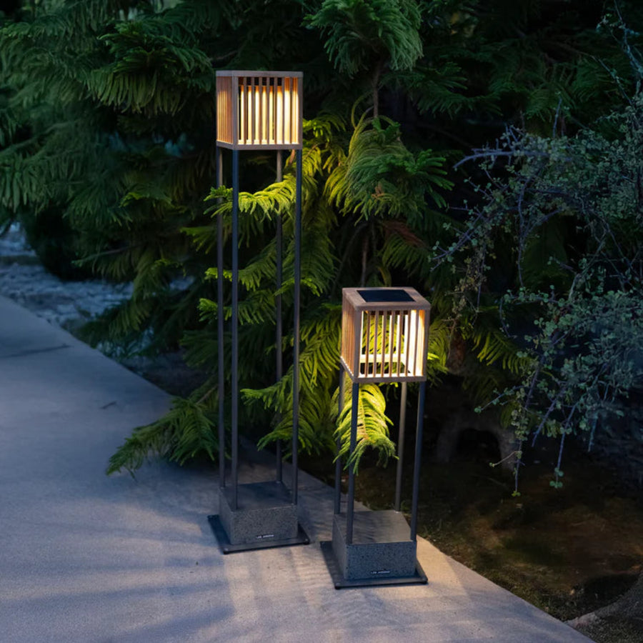 Two solar-powered outdoor floor and table lamps on a patio with greenery in the background by Les Jardins available at Spacio retail stores in Mumbai & Kolkata.  