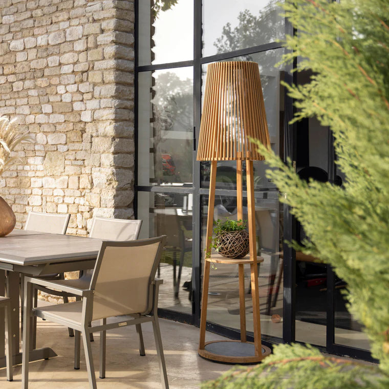 Wooden floor lamp cum side table in an outdoor setting with a stone wall and patio furniture  by Les Jardins available at Spacio retail stores in Mumbai & Kolkata. 