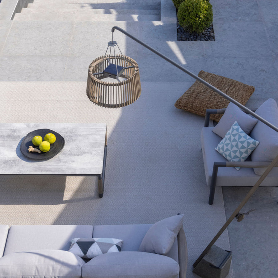 Outdoor patio on a sunny day with gray sofa, coffee table, and outdoor floor lamp by Les Jardins available at Spacio retail stores in Mumbia & Kolkata. 