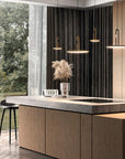Modern kitchen interior with a large wood island, dark curtains, hanging pendant lights, a bar stool, and a view of trees through a window.