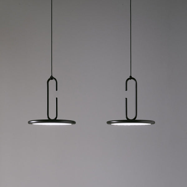 Two modern pendant lights with black metal U-shaped frames and circular shades, suspended against a plain gray background.