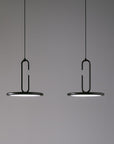 Two modern pendant lights with black metal U-shaped frames and circular shades, suspended against a plain gray background.