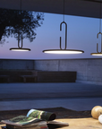 Three modern pendant lights with black metal frames and glowing white diffusers hang over a table in an outdoor patio setting at dusk.