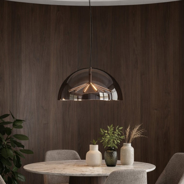 A modern semi-dome pendant light with a dark smoked glass shade and a warm glowing geometric metal interior, hanging above a dining table in a contemporary room with dark wood paneling.