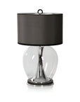 Table lamp with a black shade and clear glass base on a white background from Pieter Adam available at Spacio in India. 