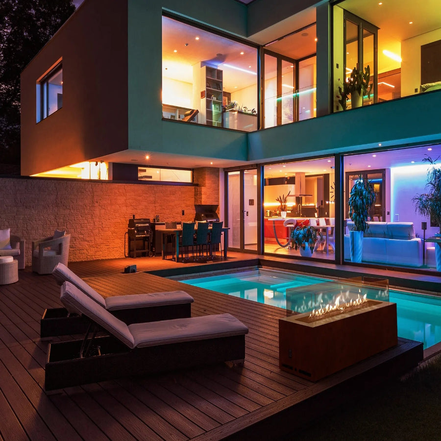 Modern house exterior with pool, lounge chairs, and fire pit at night.
