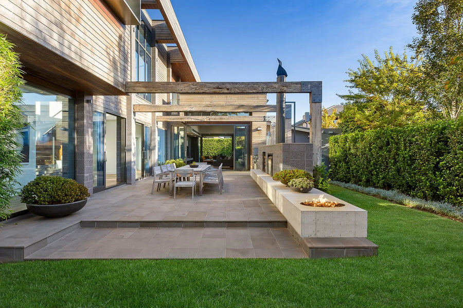 Modern outdoor patio with a fire pit, chairs, and a view of a house.