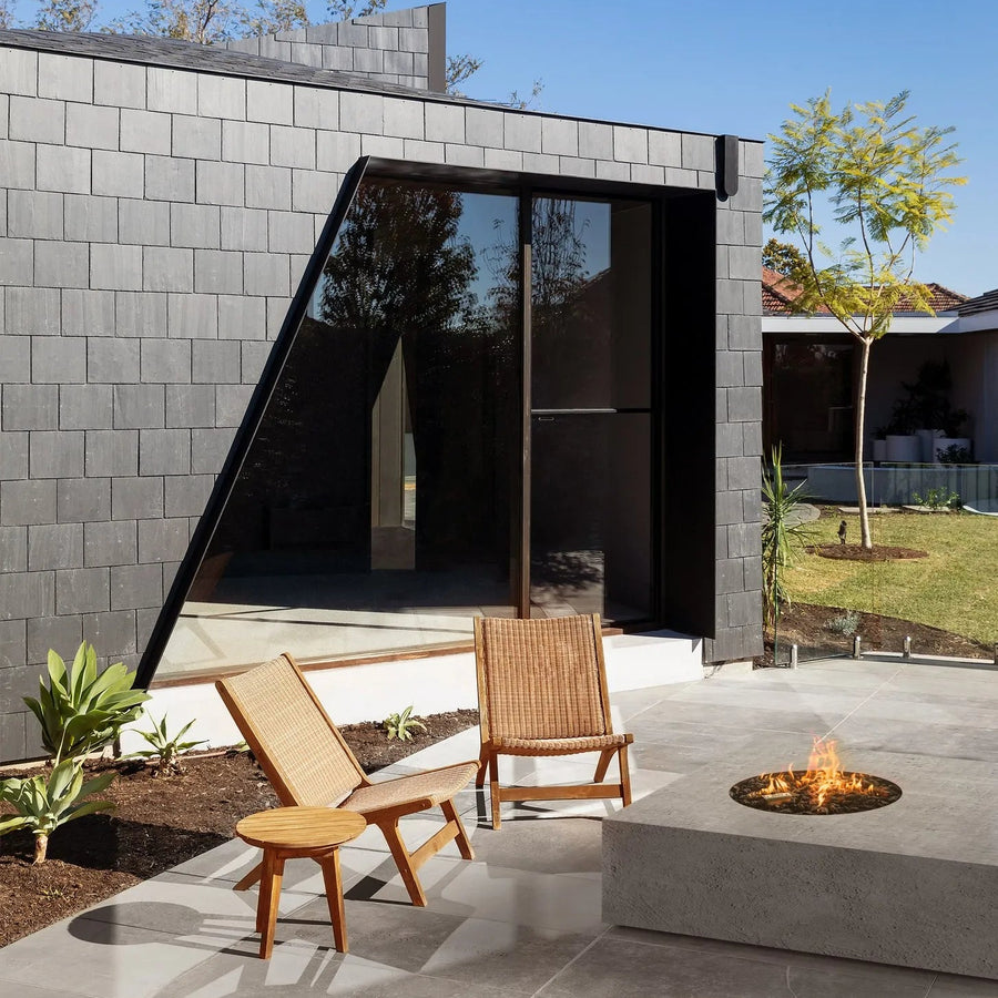 Modern outdoor setting with a fire pit, chairs, and a building with a glass wall.