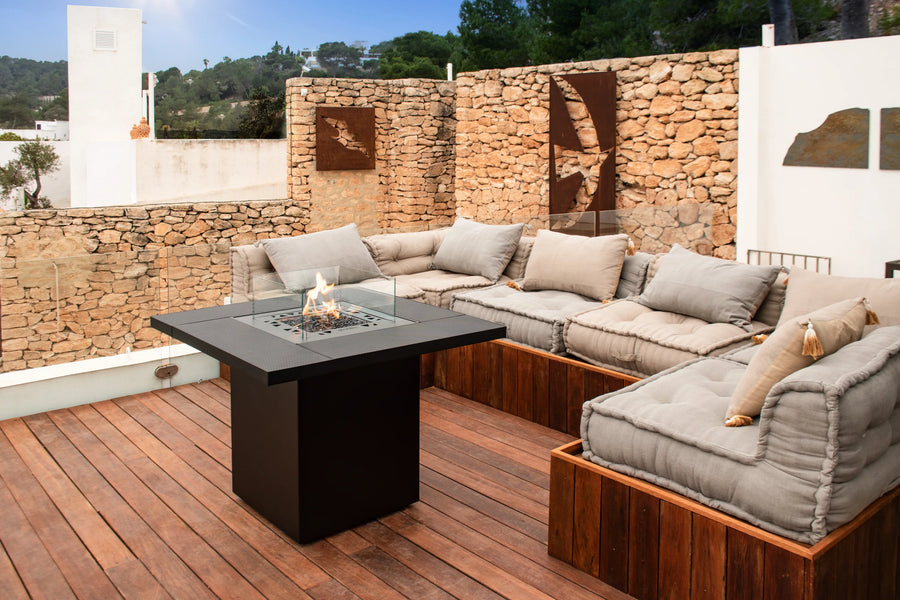 Outdoor patio with sectional sofa and fire pit table against a stone wall.