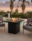 Outdoor patio setup with fire pit table, chairs, and decorative pillows by a pool.
