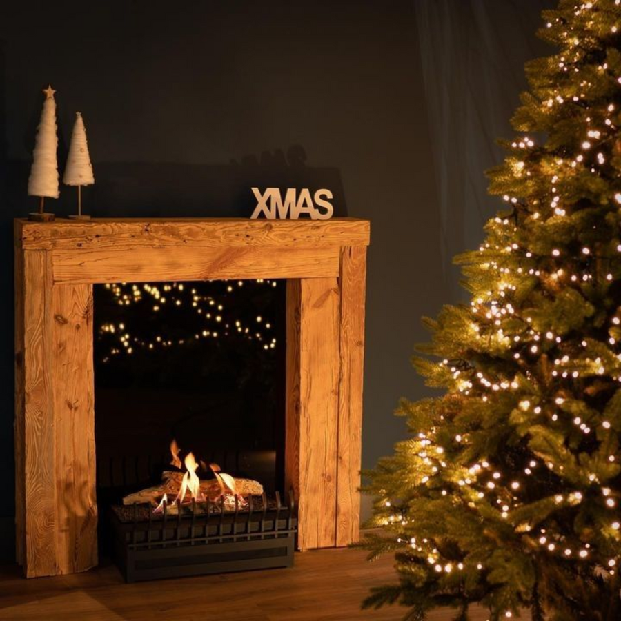 Planika Basket fire place with logs in a wooden fireplace mantle with christmas tree and decorations. 
