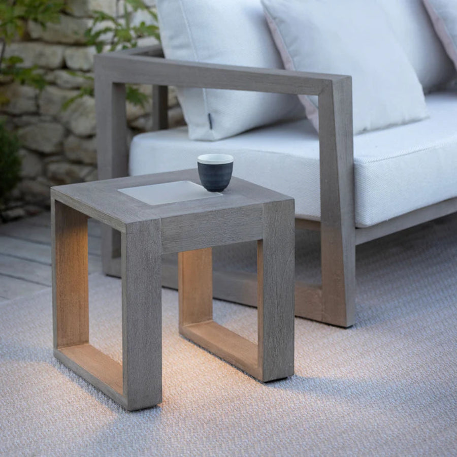 Outdoor setting with a weathered teak side table with solar light and a white sofa by Les Jardins available at Spacio retail stores in Mumbai & Kolkata. 