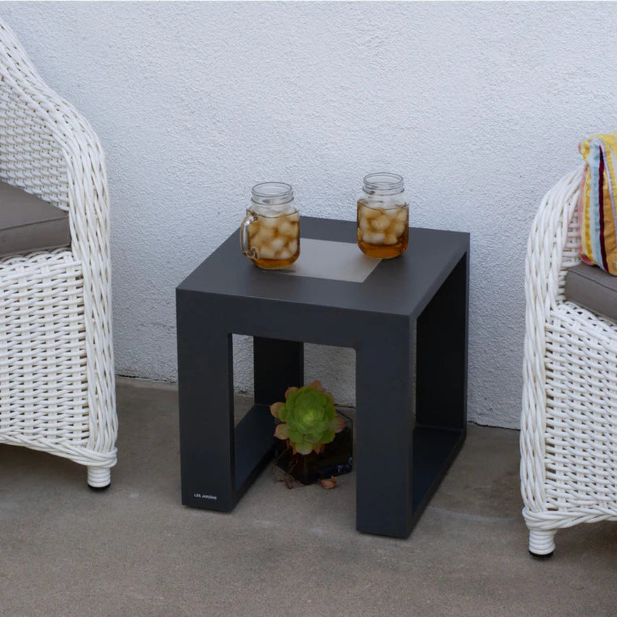 Black solar light side table with two jars of iced tea between two white wicker chairs against a light gray wall by Les Jardins available at Spacio retail stores in Mumbai & Kolkata. 