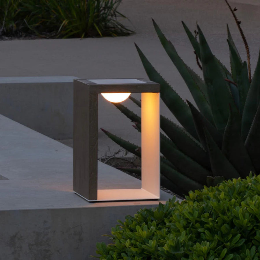 Modern outdoor indoor solar lantern with a concrete base and glass cover, illuminated in a garden setting  by Les Jardins available at Spacio retail stores in India.