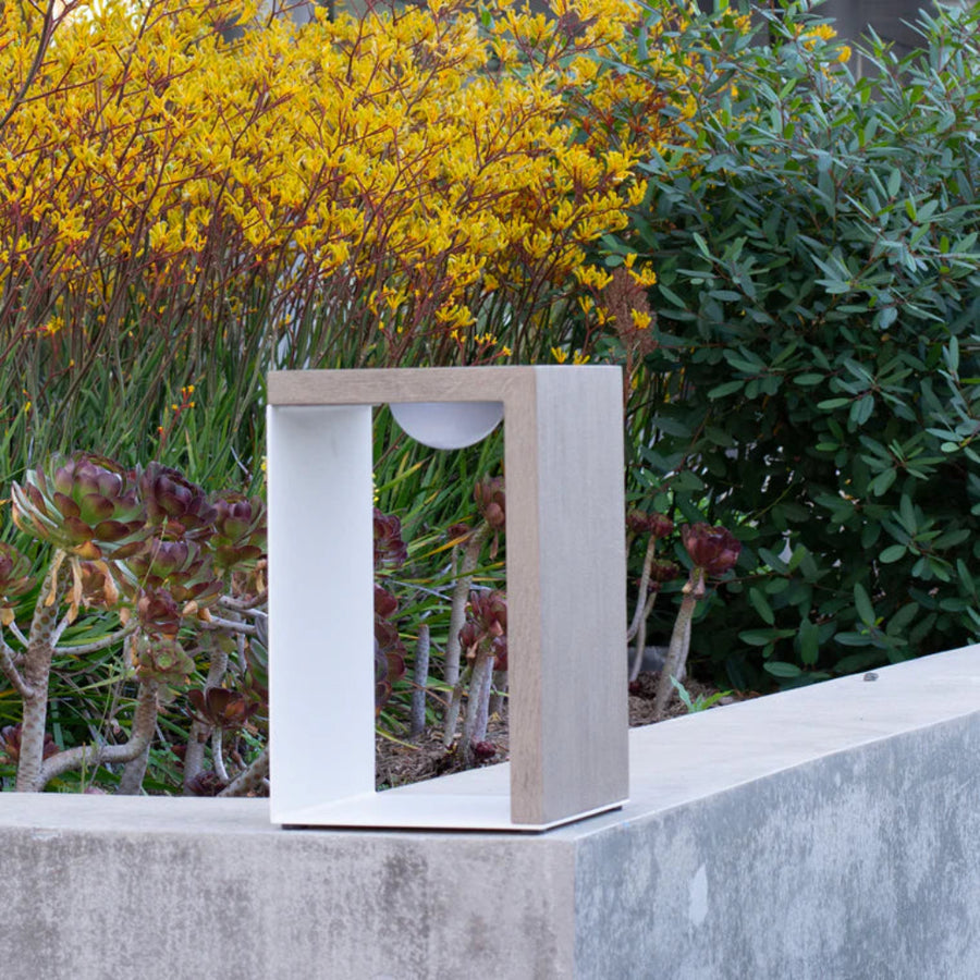 Modern outdoor solar lantern on a concrete surface with greenery and yellow flowers in the background by Les Jardins available at Spacio retail stores in India.