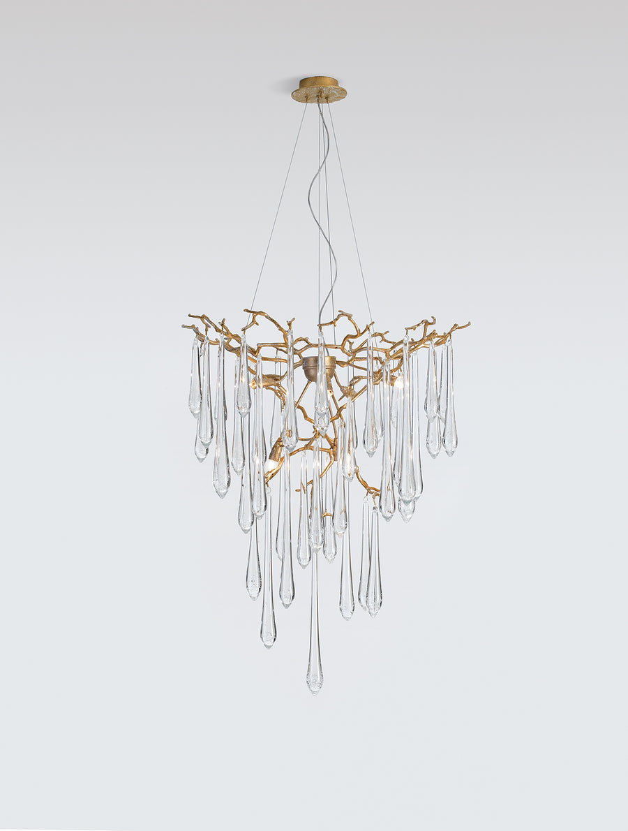 A Serip Aqua Chandelier from the Serip brand, crafted with gold and crystal materials, hangs elegantly from a white wall.