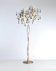 A floor lamp with glass droplets hanging from golden branch on a light grey colour background