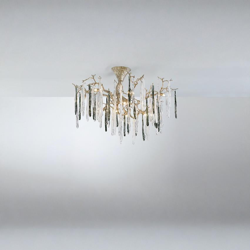 A chandelier suspended from a ceiling with colourful glass icicles hanging from golden colour branches on a dark grey background.