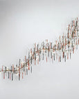 A grand wall light installation with colourful glass icicles hanging from metal branches in the shape of a wave on the wall on a light grey colour background. 
