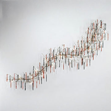 A grand wall light installation with colourful glass icicles hanging from metal branches in the shape of a wave on the wall on a light grey colour background. 