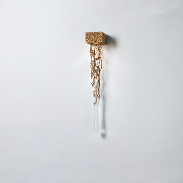Decorative wall light with gold branches and crystal shaped like a water drop on a white background