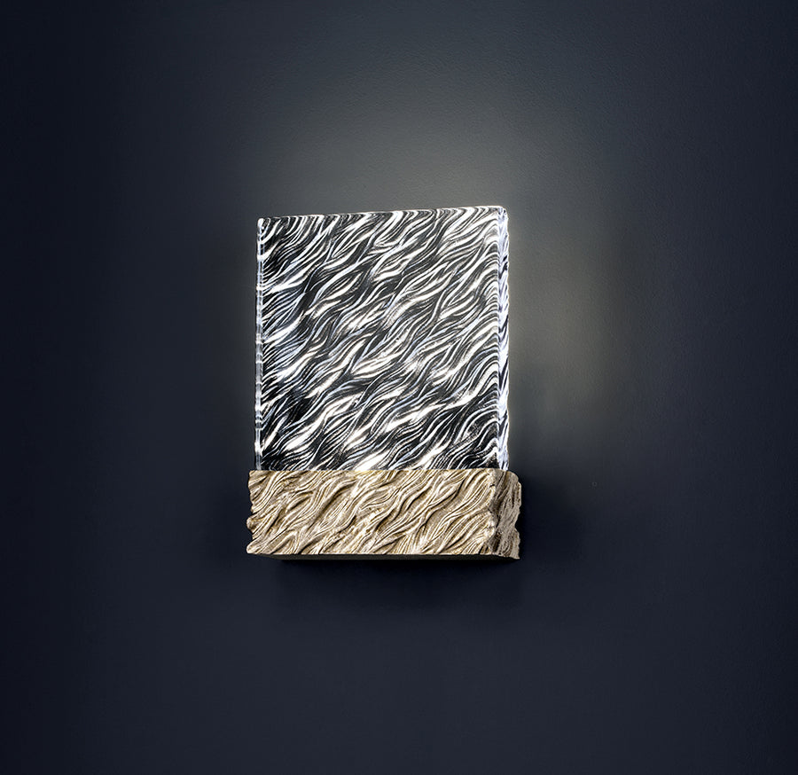 Decorative wall light with patterned glass top and textured gold base on a dark background
