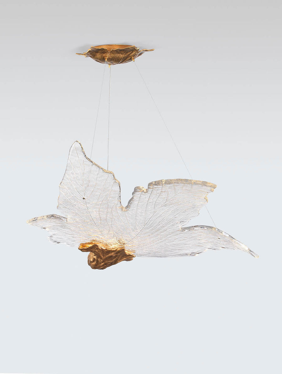 Decorative sculptural hanging light in leaf shape made of brass and glass with gold accents on a white background