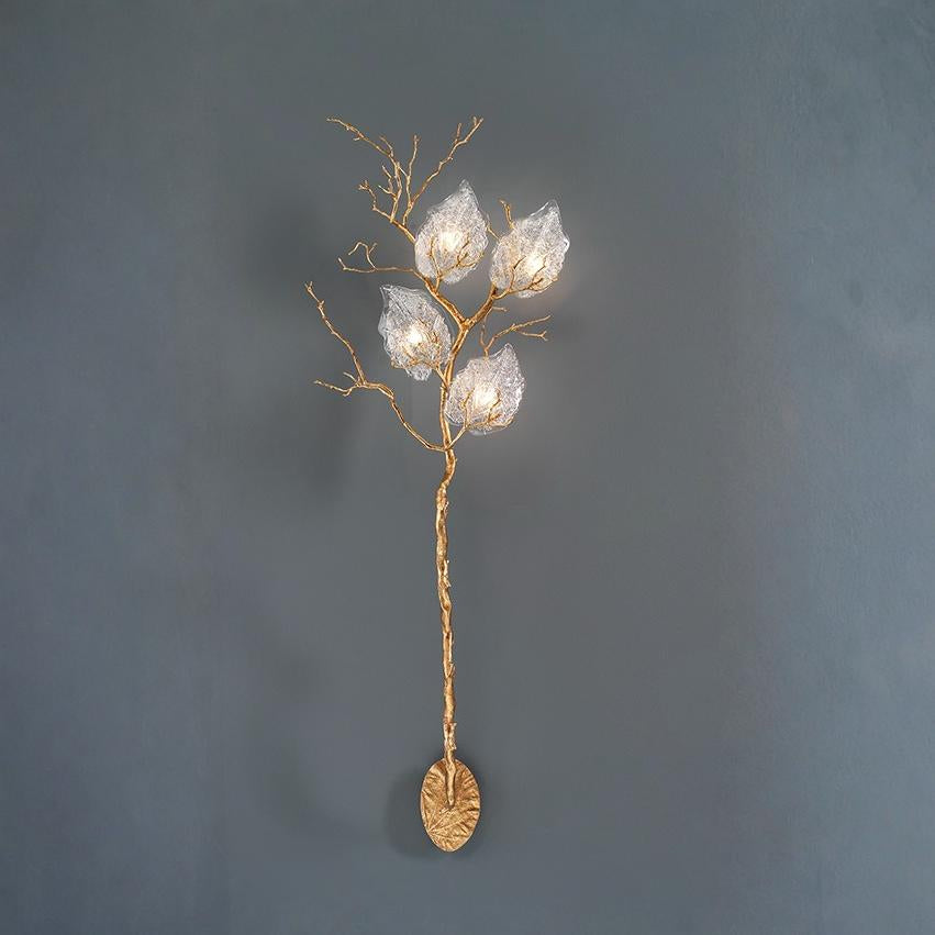 Decorative wall light fixture with gold branch and glass shades on a dark gray background