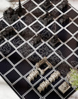 A close-up of Indian monuments chessboard with black squares, white grid lines, and miniature dark stone towers and silver castle pieces arranged on a light marble surface.