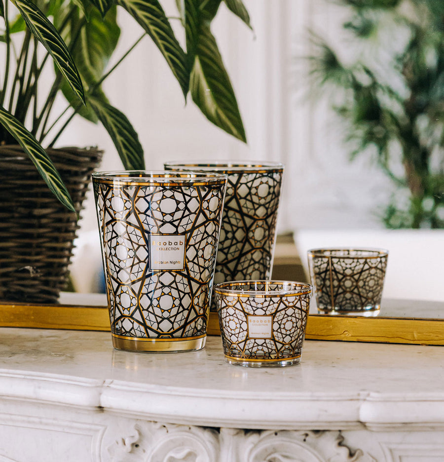 A set of Baobab Arabian Nights scented candles on a table next to a potted plant, emanating a captivating fragrance.