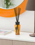 Baobab Curi De Russie Diffuser 500ml DIF500CUR by Baobab, a home fragrance diffuser with an orange scent, is placed on a table beside a mirror.