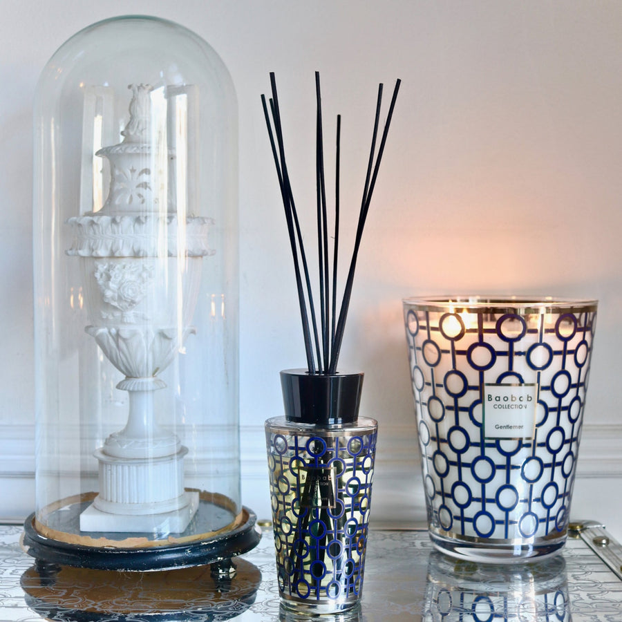 A table adorned with Baobab Gentlemen Diffuser 500ml DIF500GEN and scented candles emitting a delightful rum fragrance.