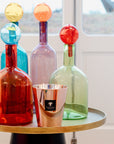 Four Baobab Roseum Candle MAX16ROS decanters filled with fragrances on a table in front of a window, exuding femininity.