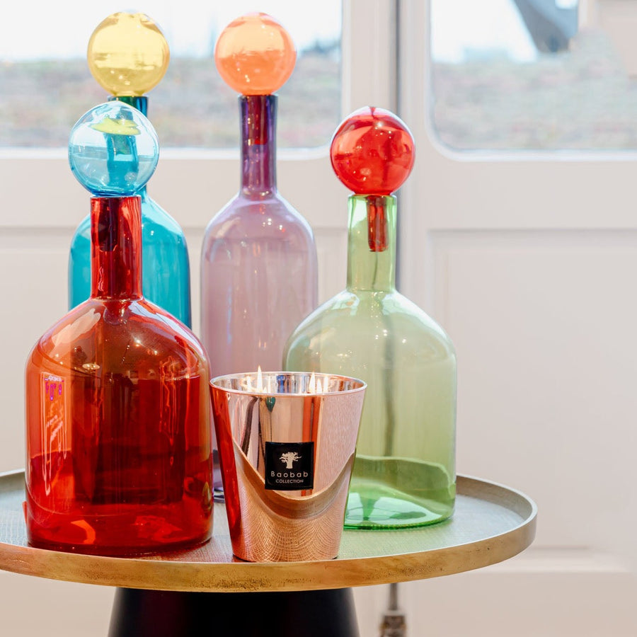 Four Baobab Roseum Candle MAX16ROS decanters filled with fragrances on a table in front of a window, exuding femininity.