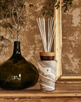 Baobab Sand Siloli 2L Diffuser Med TOTEMMSSI by Baobab, in a glass vase next to a frame, emitting fragrance and acting as a decorative object.