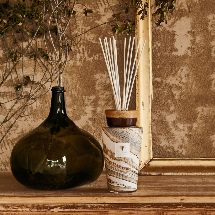 Baobab Sand Siloli 2L Diffuser Med TOTEMMSSI by Baobab, in a glass vase next to a frame, emitting fragrance and acting as a decorative object.