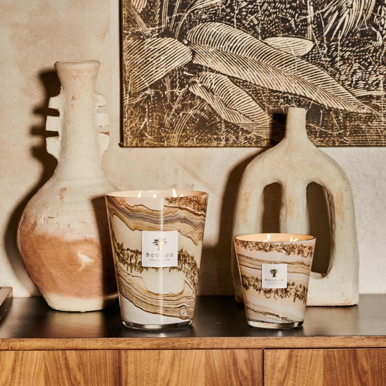 A collection of Baobab Sand Siloli candles on a shelf next to a painting.