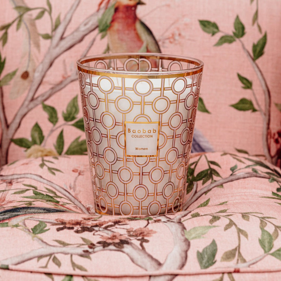 A Baobab Women Candle MAX16WOM sitting on a pink chair, symbolizing support for the Breast Cancer Foundation and women's health, with delicate bird designs.