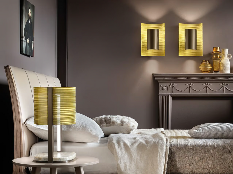 A bedroom with a yellow Masiero Ebe Wall Sconce from the Masiero Ebe Collection, illuminating the space with its luxury lighting and creating a cozy atmosphere alongside a fireplace.