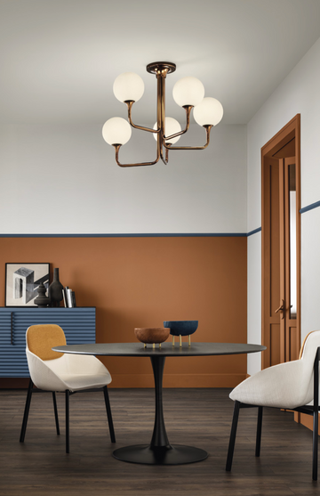 A dining room with orange walls and chairs featuring decorative Masiero Tee Chandeliers for luxury lighting.
