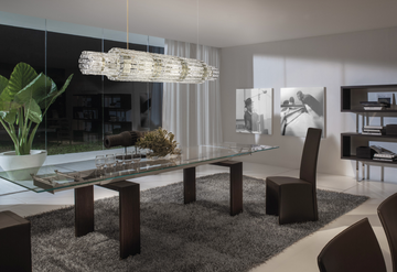 A modern dining room with a glass table and chairs featuring the Masiero Vegas Chandelier by Masiero lighting.