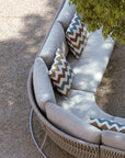 The Sifas Basket Sofa Collection, designed by Sifas, is an outdoor furniture basket collection featuring a white couch with pillows. It is specifically designed with waterproof properties for outdoor use. The couch is placed against a backdrop of a majestic tree in the background.