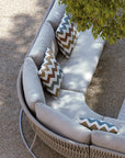 The Sifas Basket Sofa Collection, designed by Sifas, is an outdoor furniture basket collection featuring a white couch with pillows. It is specifically designed with waterproof properties for outdoor use. The couch is placed against a backdrop of a majestic tree in the background.