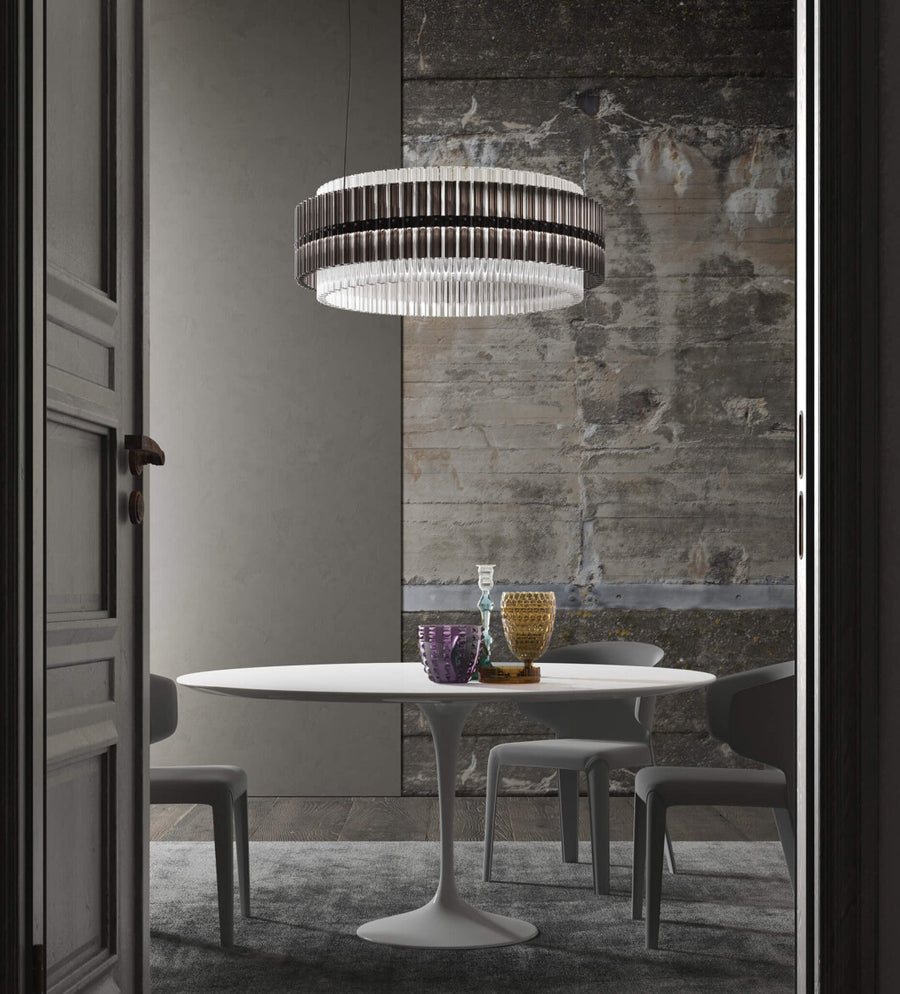 A round chandelier installation in smoke and clear glass in above a round dining table in a modern theme interior of a luxury home. Discover the Carmen collection by Italamp – Italian Murano glass lighting in clear, smoke, and teak finishes. Elegant designs for luxurious interiors.

