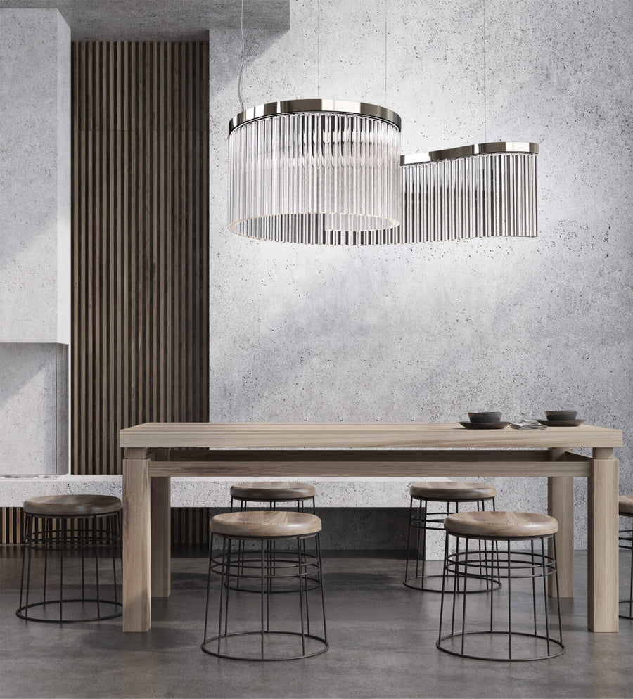 Discover the Carmen collection by Italamp – Italian Murano glass lighting in clear, smoke, and teak finishes. Elegant designs for luxurious interiors. A spiral chandelier in a clear finish on a wooden dining table in a minimal japandi theme interior